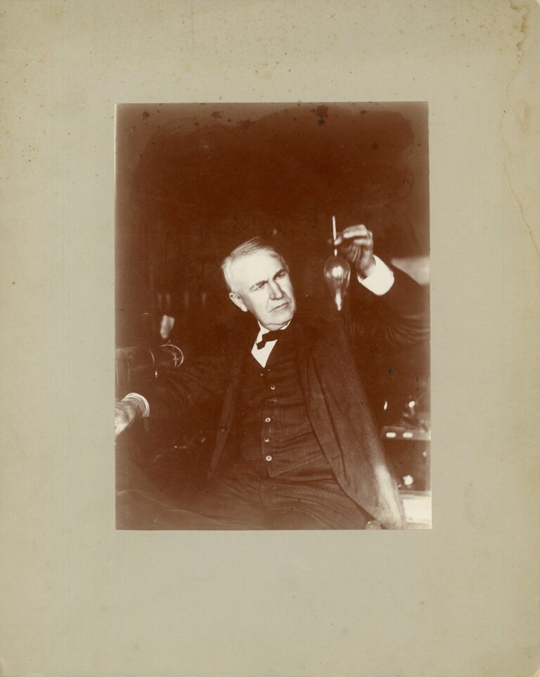 Thomas Edison holding a small electric lamp or test tube in his laboratory in 1905