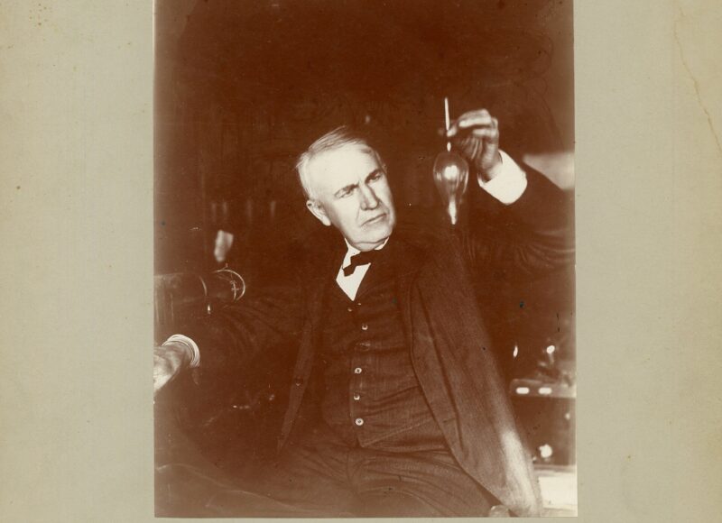 Thomas Edison holding a small electric lamp or test tube in his laboratory in 1905